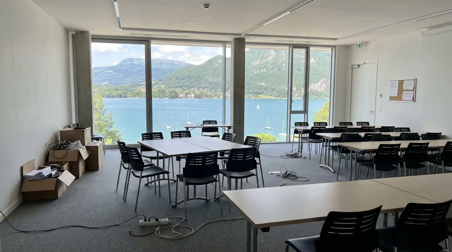 Salle de séminaire modulable vide en cours de reconfiguration entre formats plénière et ateliers, lumière naturelle abondante